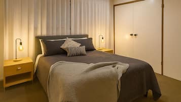 A neatly arranged bedroom with a bed, bedside lamps, a nightstand, and a wardrobe.