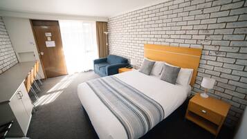 Habitación de hotel con una cama grande, cabecero de madera, un sillón azul, un escritorio con silla y pared con diseño de ladrillo.