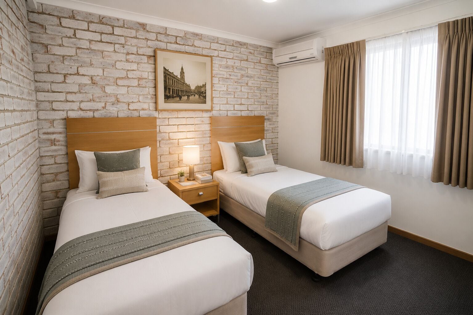 A hotel room with two beds, a brick wall, a framed picture, an air conditioning unit, and a window with curtains.