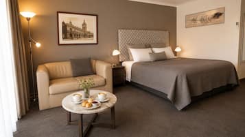 A hotel room with a bed, a sofa, a small table with a vase and pastries, and a lamp.
