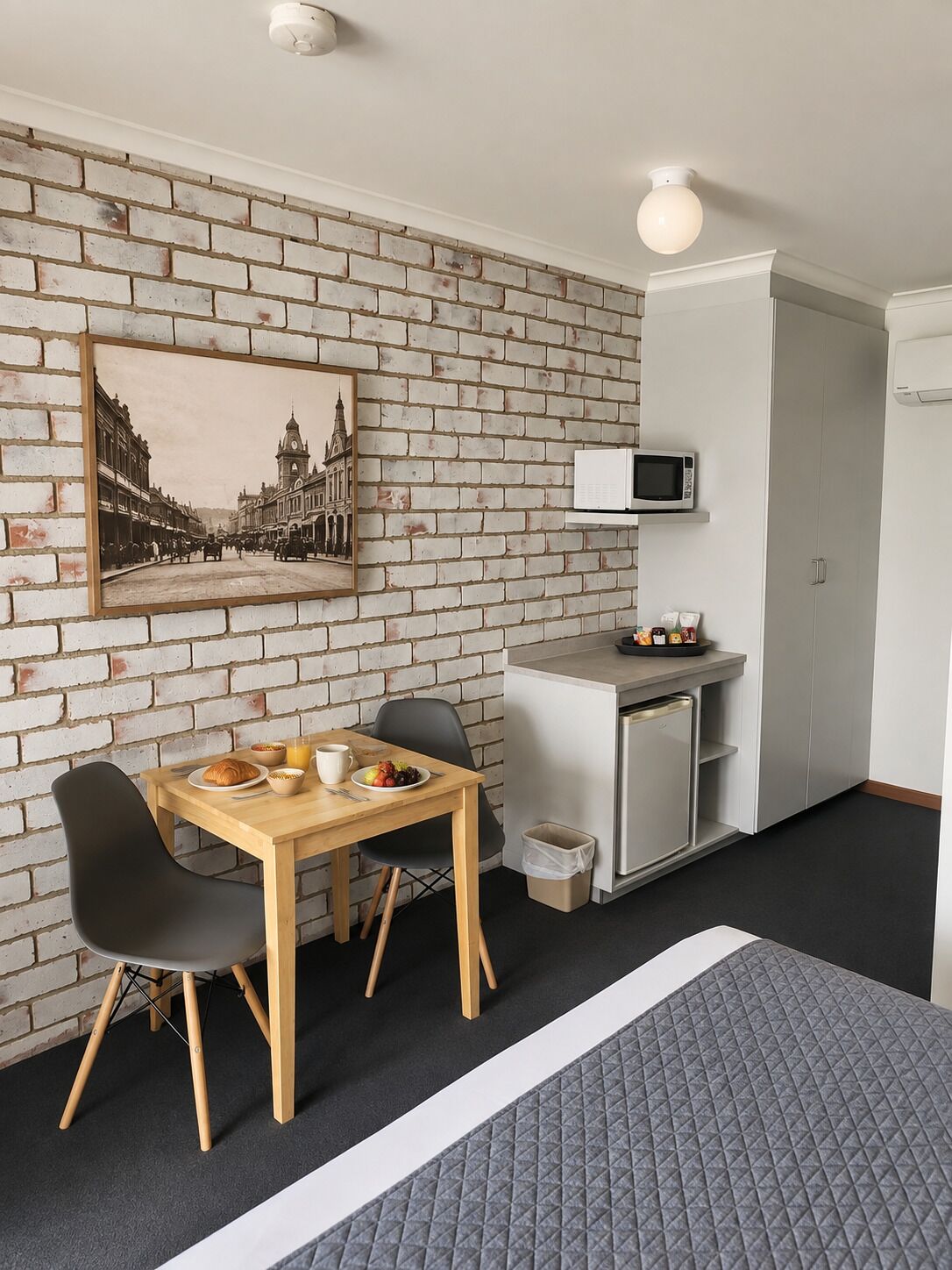 A compact room with a brick wall, a dining table with chairs, a microwave, and a small kitchenette.