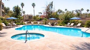 A swimming pool with lounge chairs and umbrellas, surrounded by palm trees and a building in the background. - Holiday Inn Express Palm-Desert by IHG (Palm Desert)