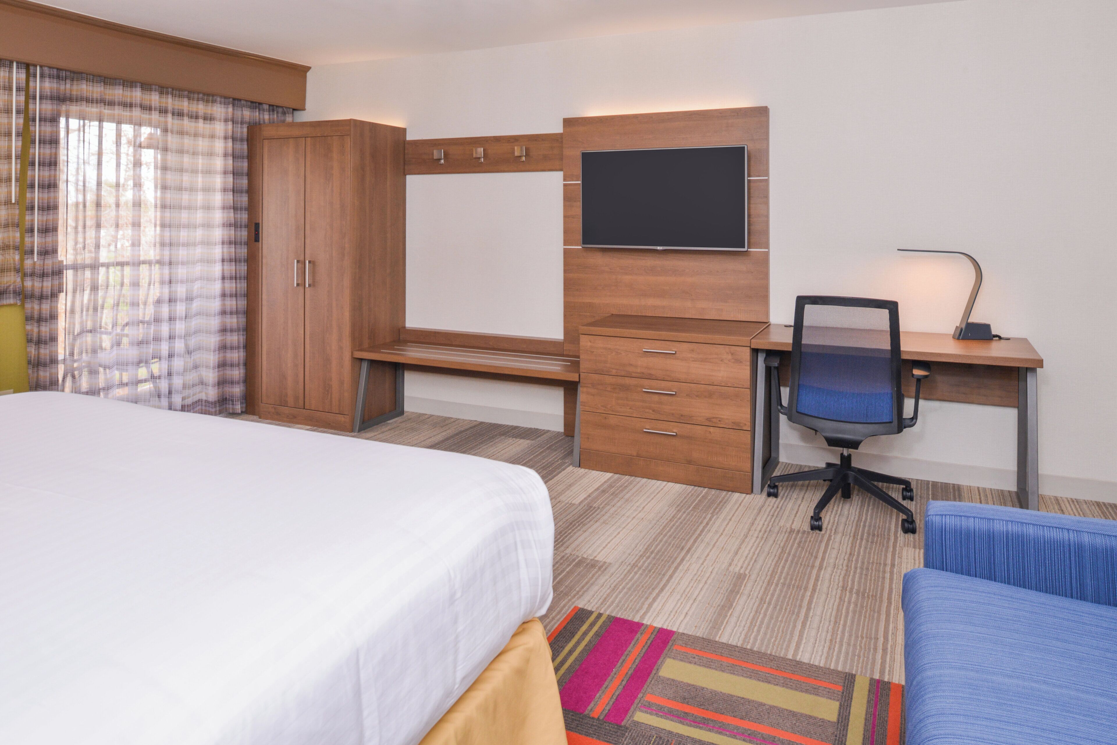 A hotel room with a bed, a desk with a chair, a television, and a wardrobe.