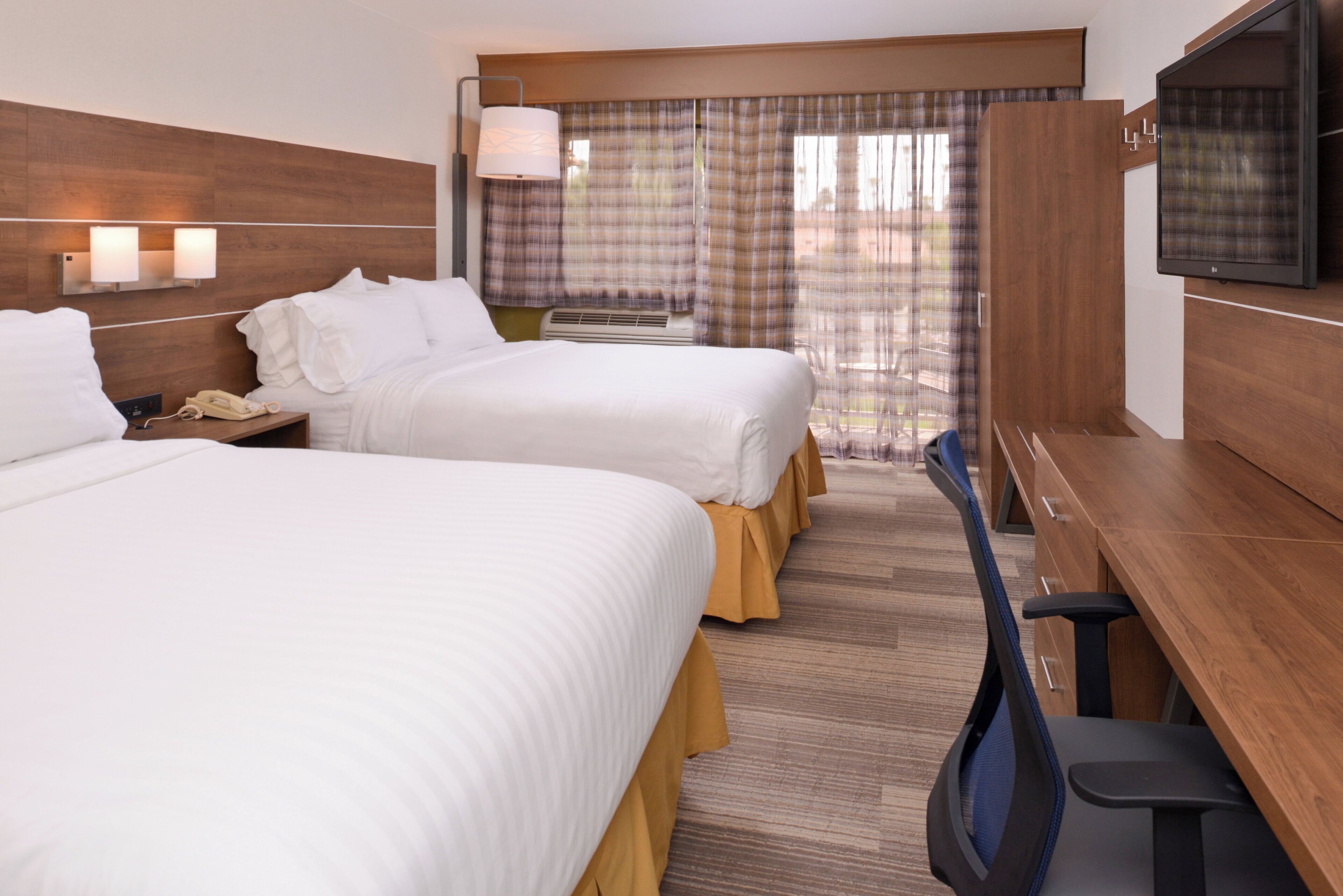 A hotel room with two beds, a desk, a chair, a television, and a window with curtains.