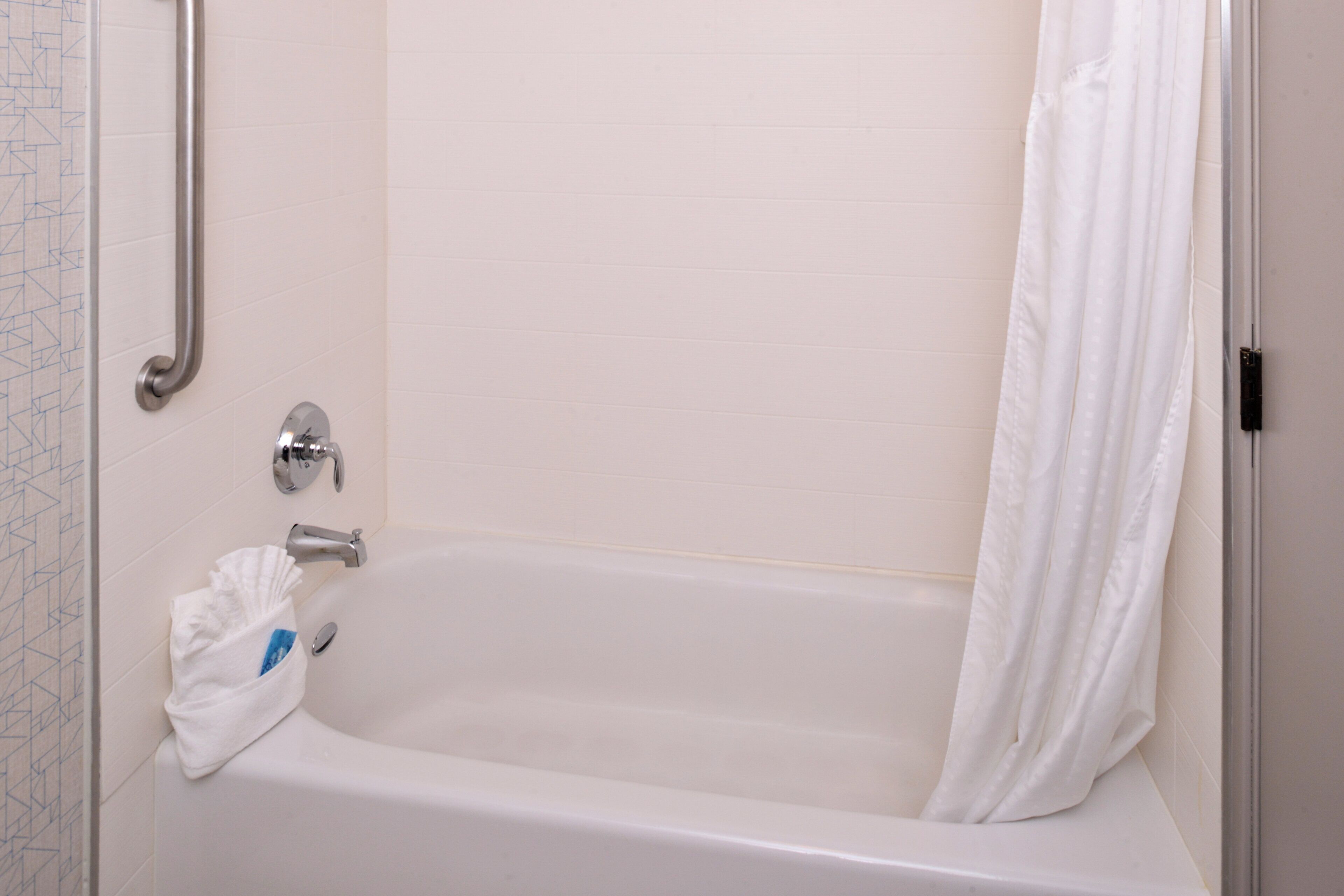 A standard white bathtub with a shower curtain, a grab bar, and a towel rack.