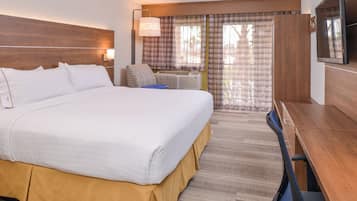 Quarto de hotel com cama grande, escrivaninha, cadeira, televisão e janela com cortinas.