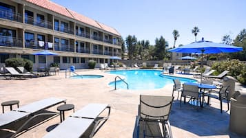 A hotel with a swimming pool, lounge chairs, and umbrellas.