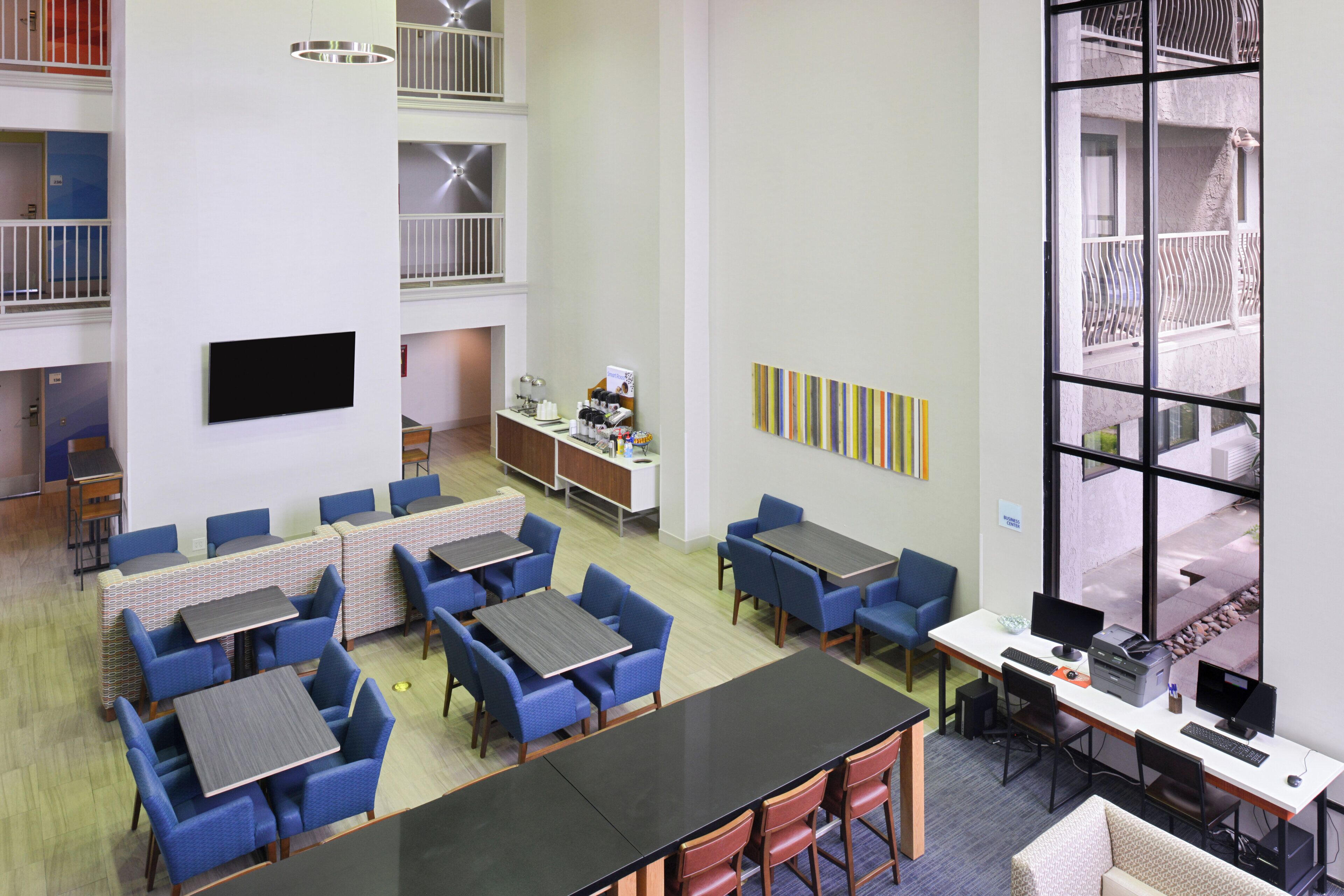 A hotel lobby with multiple seating areas, a business center, and a view of the outside.