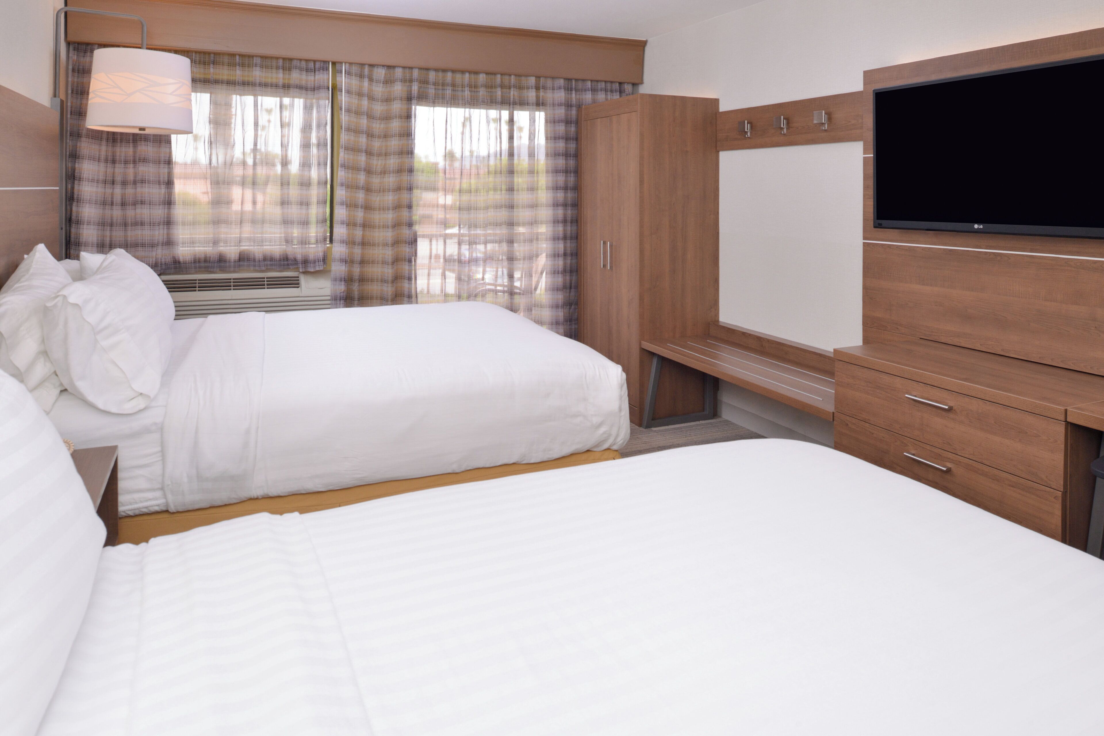 Une chambre d’hôtel avec deux lits, une télévision, une armoire et une fenêtre avec des rideaux.
