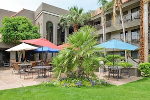 An outdoor patio area with tables and chairs, umbrellas, and a variety of plants. - Holiday Inn Express Palm-Desert by IHG (Palm Desert)