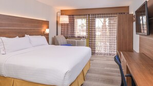 Quarto de hotel com cama grande, escrivaninha, cadeira, televisão e janela com cortinas.