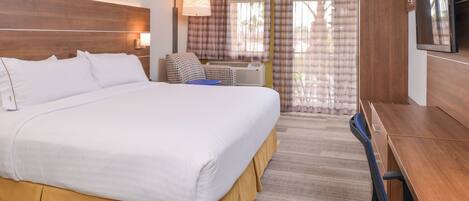 Habitación de hotel con una cama grande, un escritorio, una silla, un televisor y una ventana con cortinas.