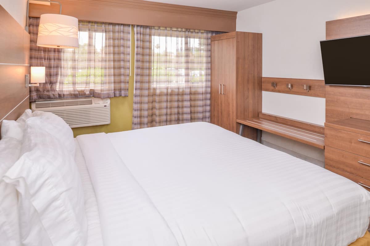 A hotel room with a bed, a TV, a wardrobe, and a window with curtains.