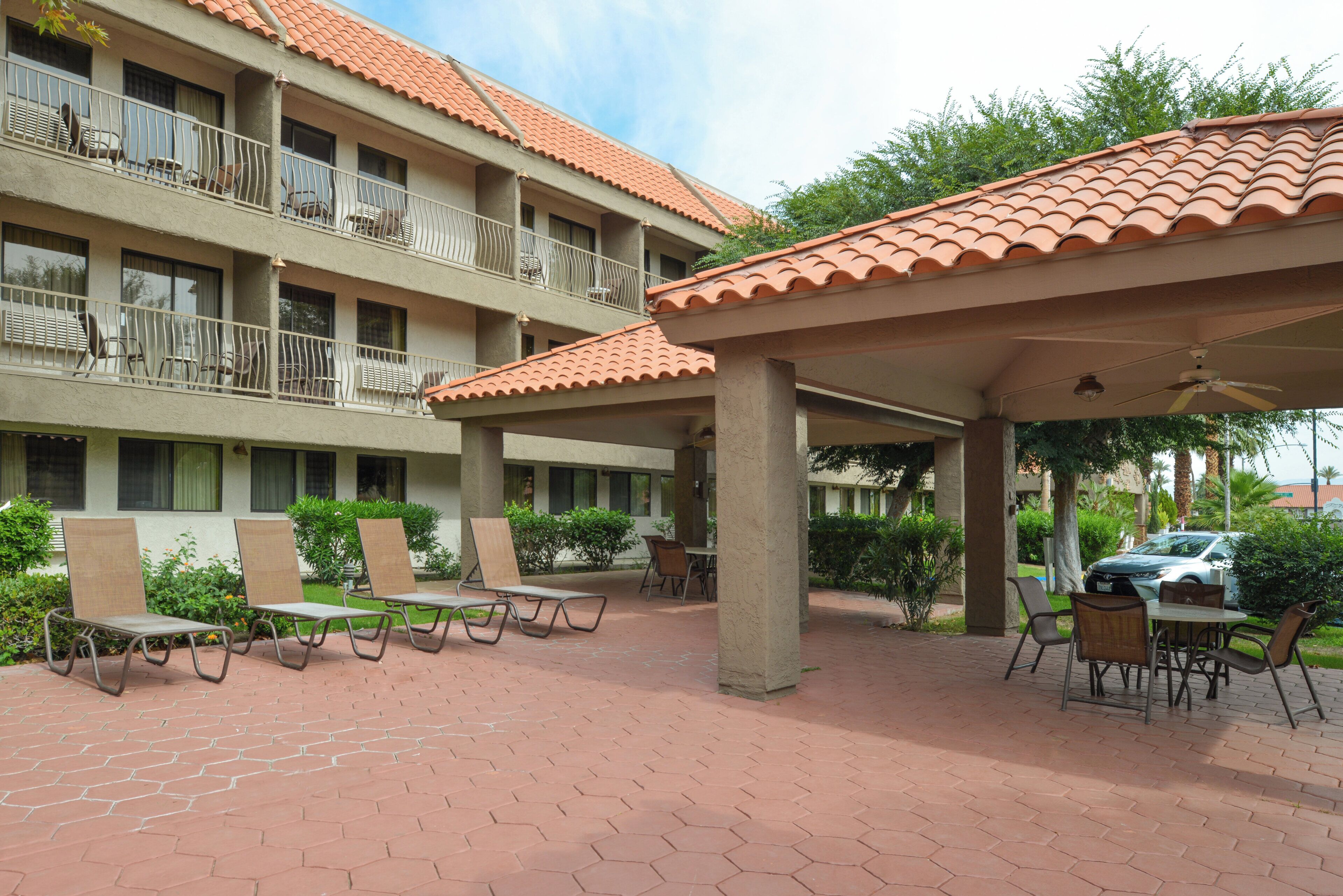A hotel courtyard with outdoor seating, covered areas, and a multi-story building with balconies.