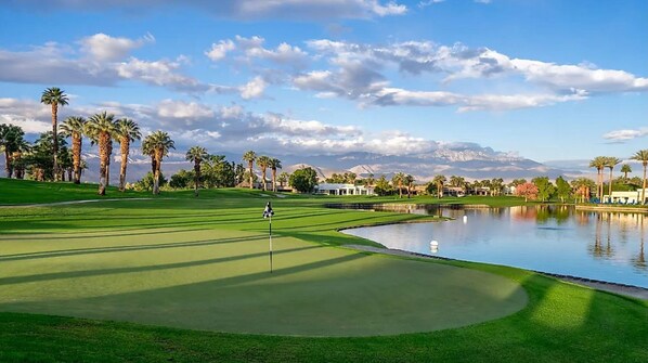 Ein Golfplatz mit Wasserhindernis, Palmen und einem Berg im Hintergrund.