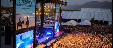 A large outdoor concert venue with a stage, audience, and tents.
