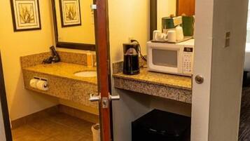 A hotel bathroom with a sink, mirror, and a microwave on the countertop.