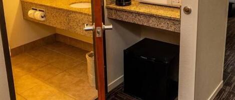 A hotel bathroom with a sink, mirror, and a microwave on the countertop.