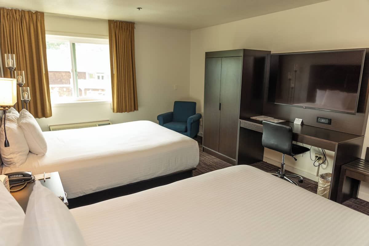 A hotel room with two beds, a desk with a telephone, a chair, a TV, and a wardrobe.