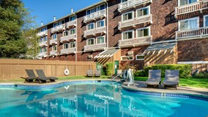 A swimming pool with lounge chairs, a wooden fence, and a brick building with balconies.