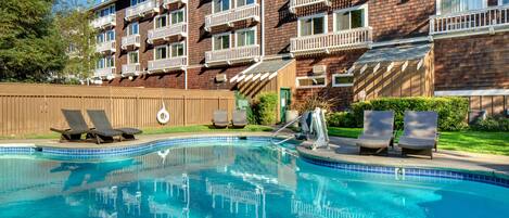 A swimming pool with lounge chairs, a wooden fence, and a brick building with balconies.