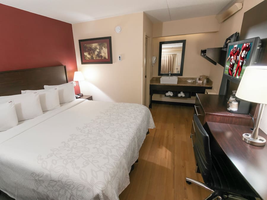 A hotel room with a large bed, a desk with a lamp, a mirror, and a television.
