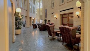 A spacious indoor area with a high ceiling, stone flooring, and a series of armchairs and tables arranged for seating. - Crockett Hotel (San Antonio)