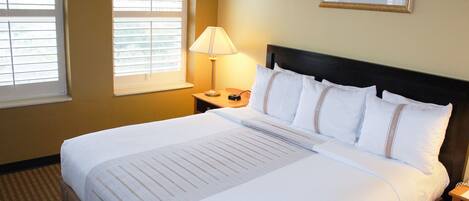 A neatly made bed with a white comforter and pillows, a bedside lamp, and a framed picture on the wall.
