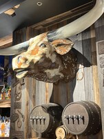 A bar area with wooden walls, a mounted cow head, and several wooden barrels with taps.