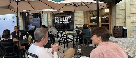 An outdoor seating area with tables and chairs under umbrellas, a brick building in the background, and a sign for 'Crockett Tavern'.