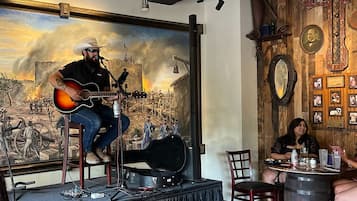 A stage with a guitar player, a mural of a battle scene, and rustic decor including wooden walls and a barrel.