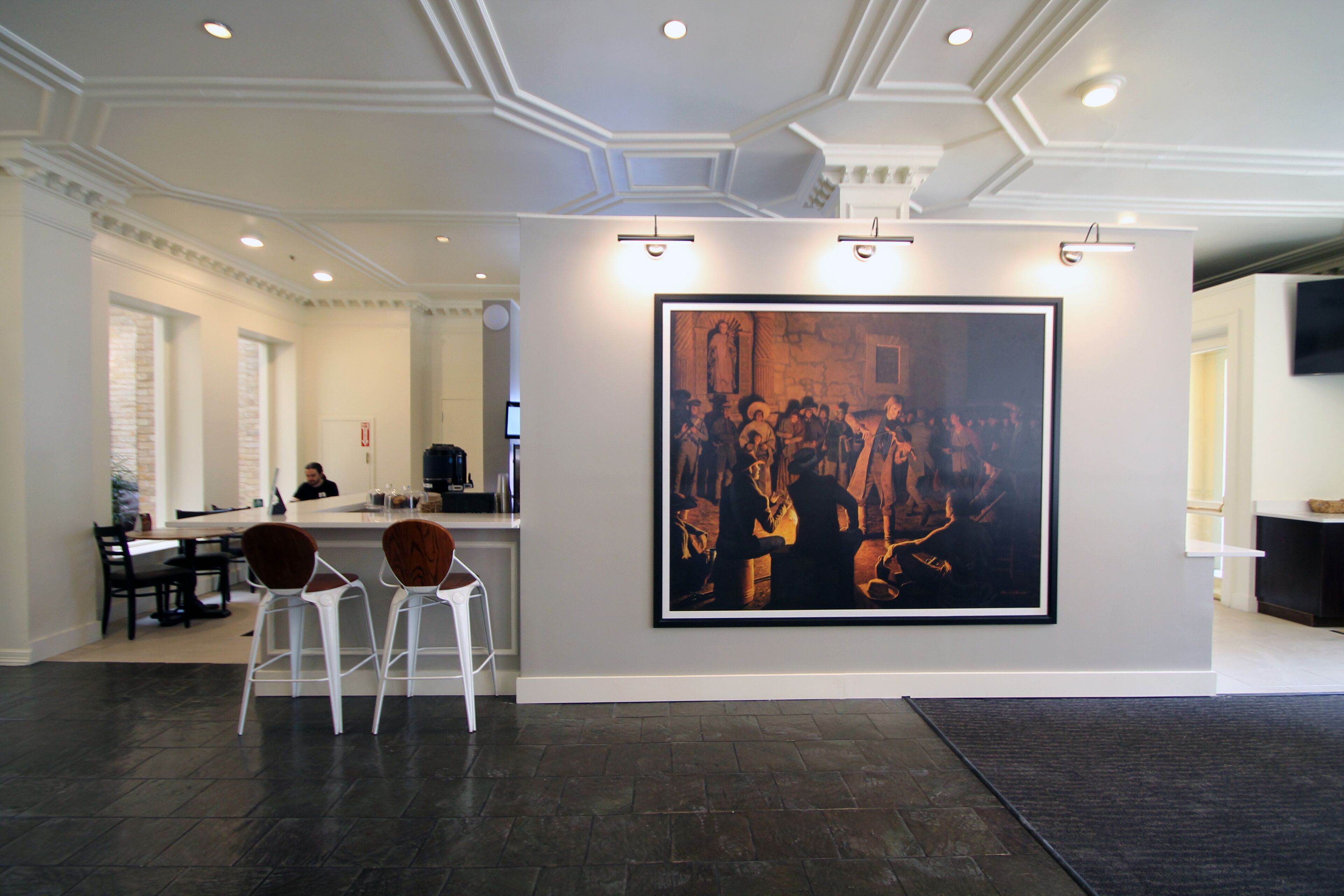 A modern interior with a large framed artwork on the wall, a bar area with stools, and a seating area with tables and chairs.