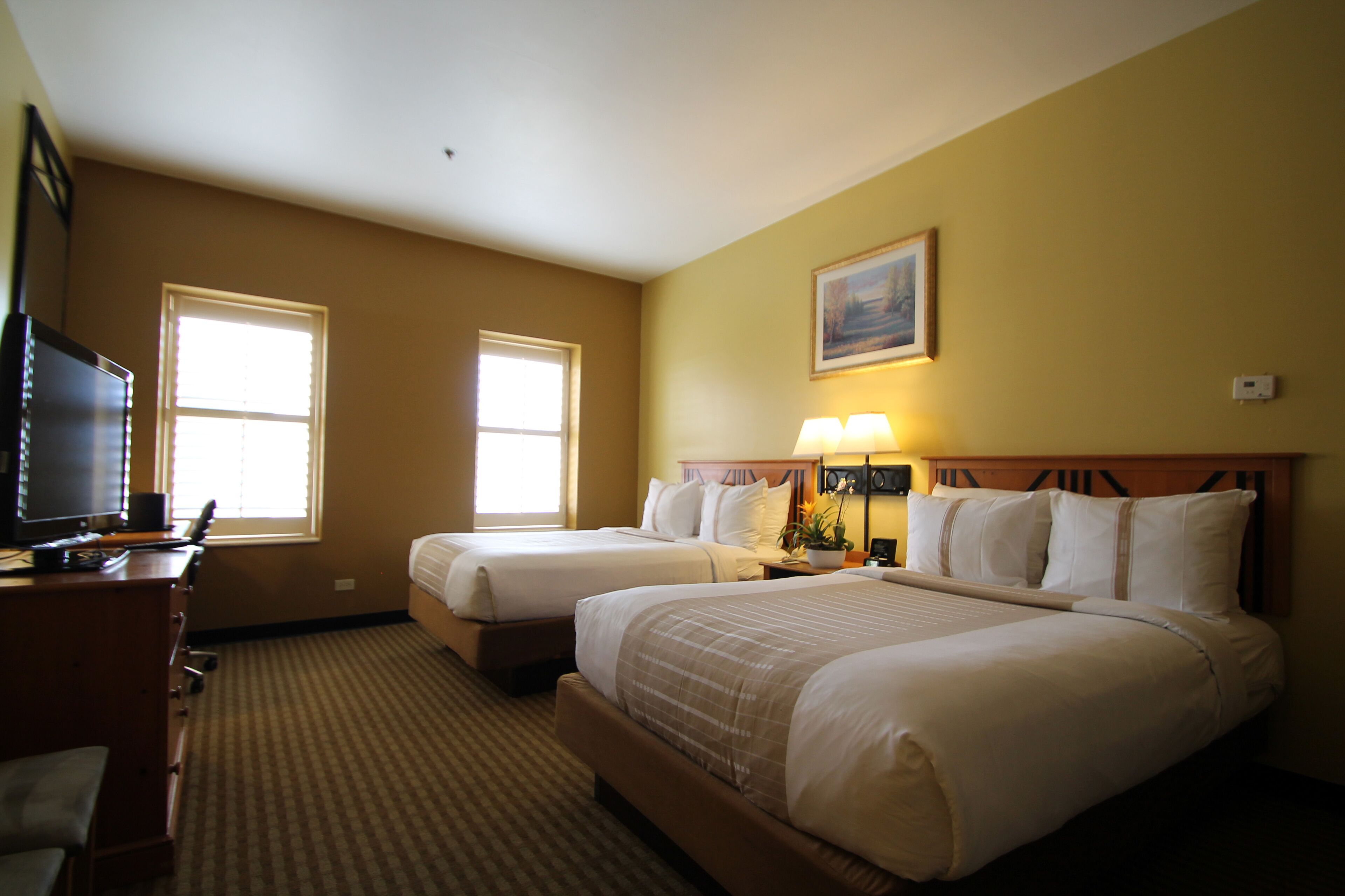 A hotel room with two beds, a desk with a computer, and two windows.