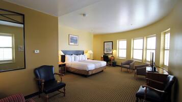 A hotel room with a large bed, two armchairs, a desk with a computer, and a TV.