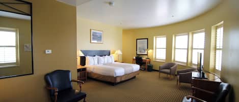 Habitación de hotel con una cama grande, dos sillones, un escritorio con una computadora y un televisor.