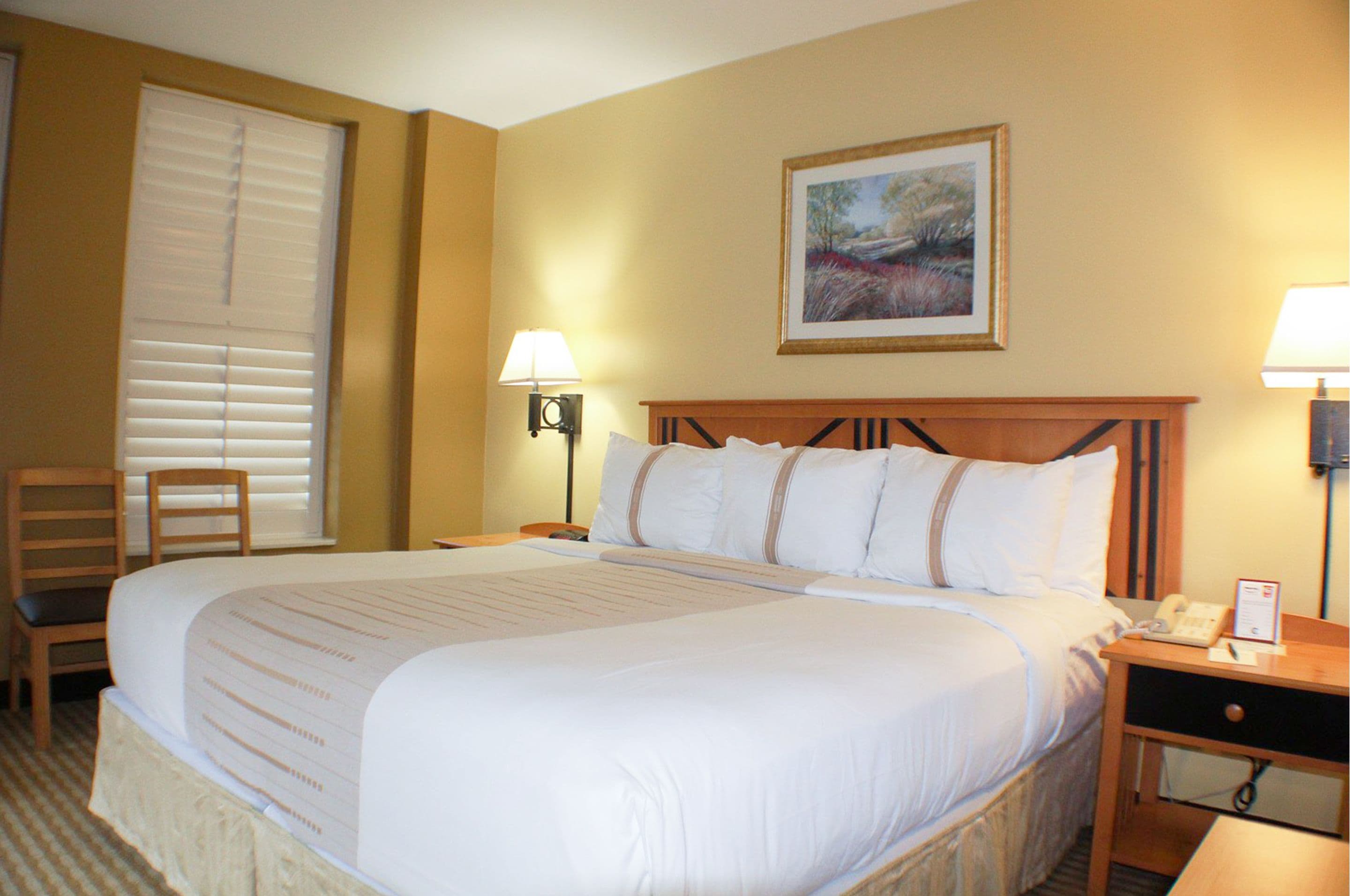 A hotel room with a large bed, two bedside tables, a chair, and a painting on the wall.