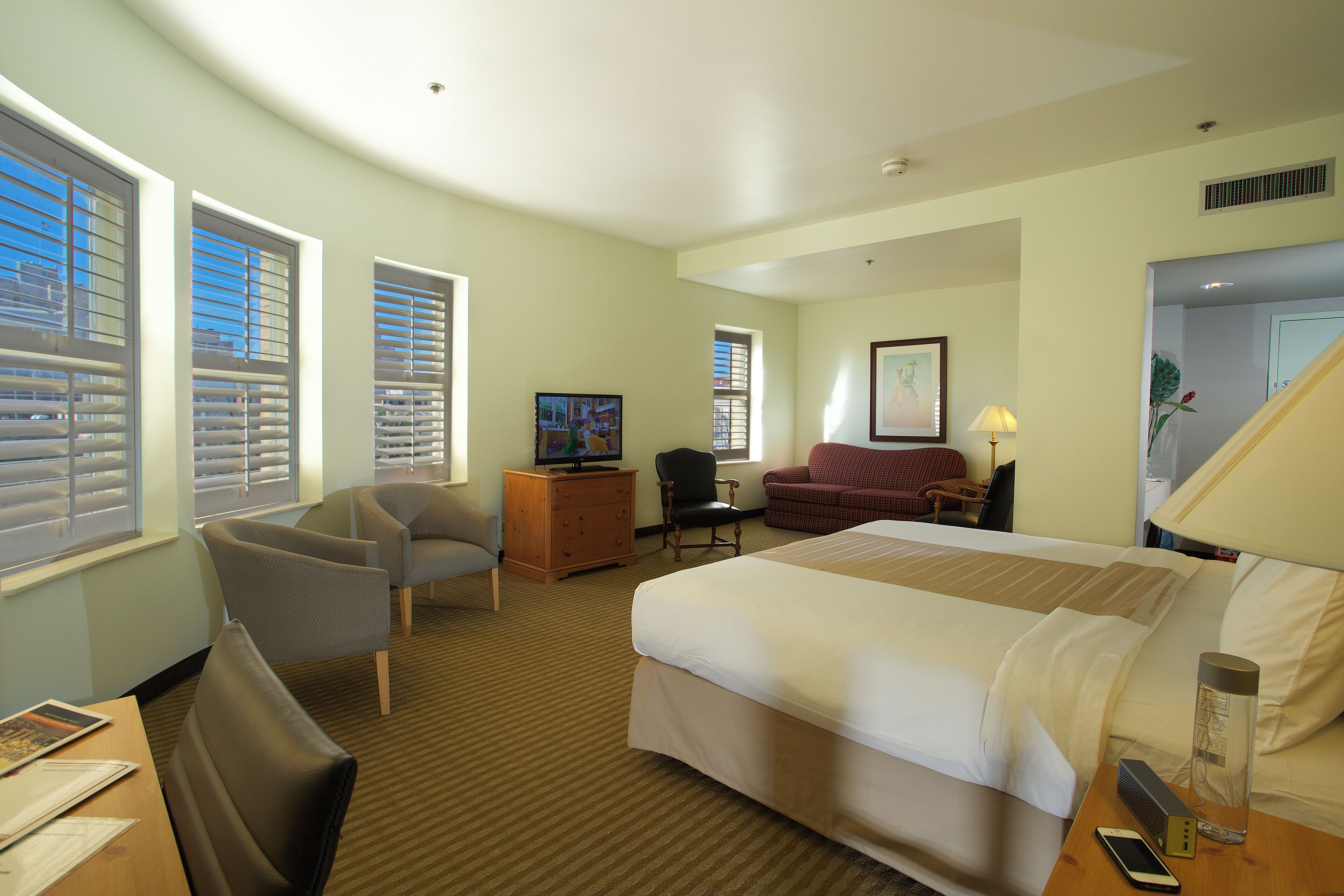 A hotel room with a large bed, a desk with a chair, a TV, and a window with blinds.