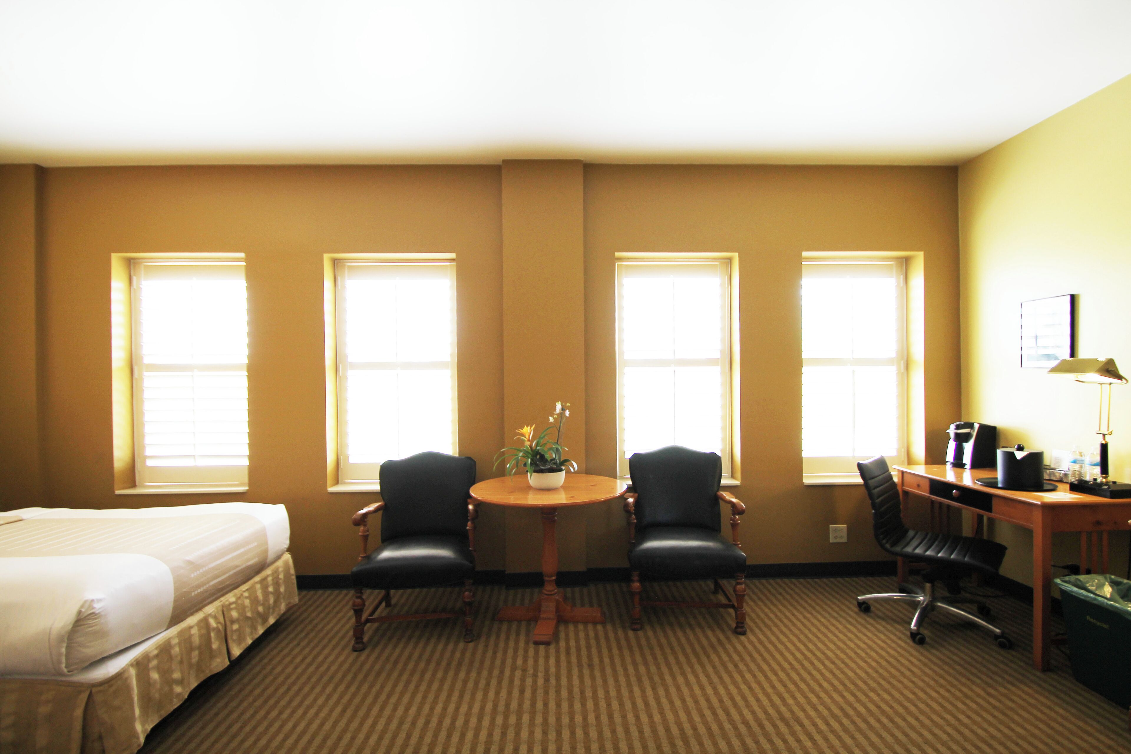 A hotel room with a bed, two chairs, a desk with a computer, and a trash bin.