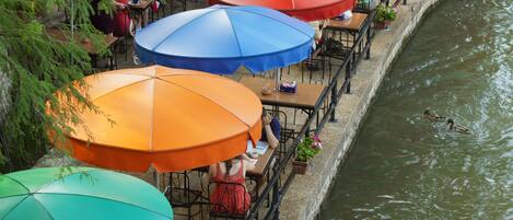 Mesas de comedor al aire libre con sombrillas a lo largo de un canal.