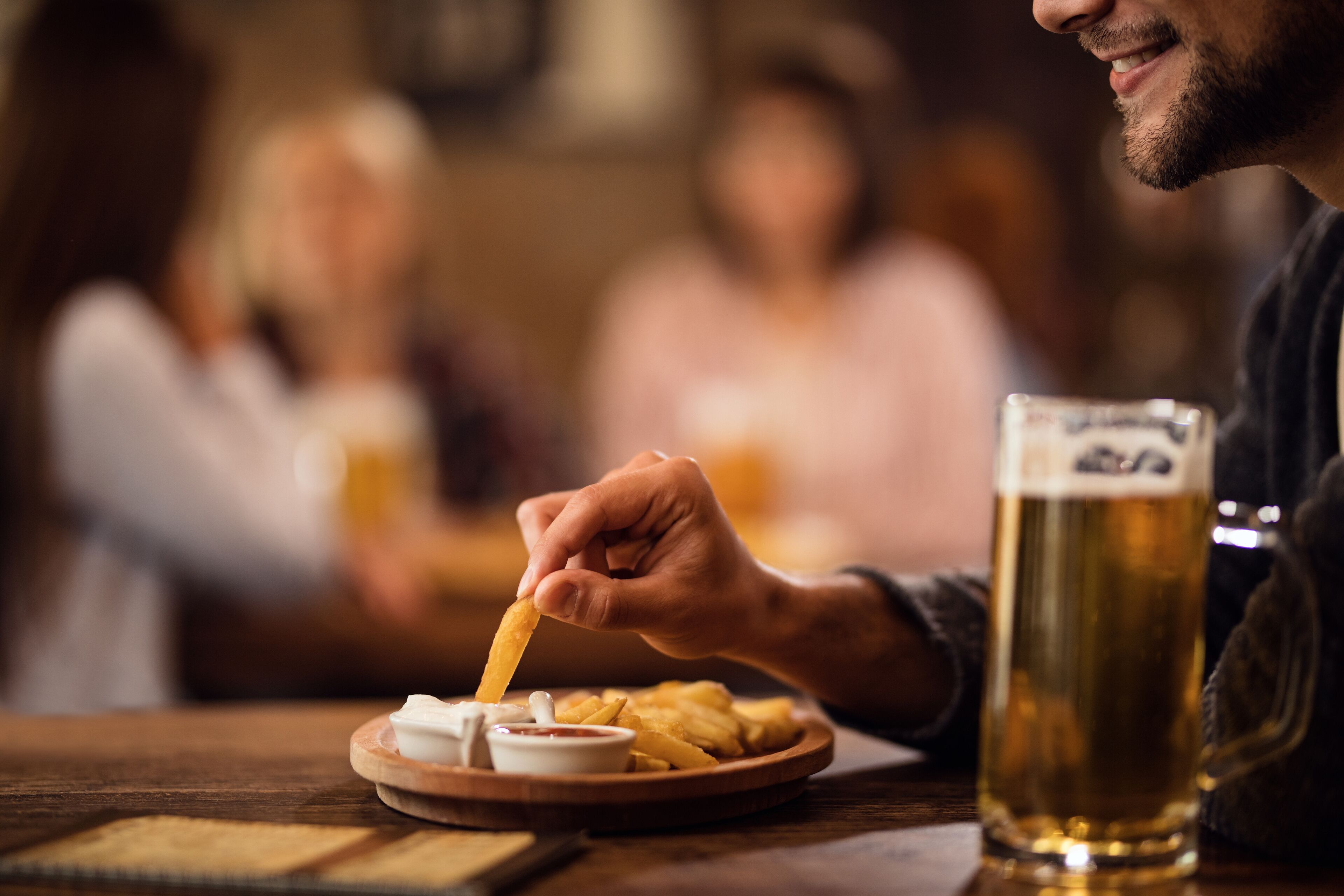 Una persona intingendo patatine fritte in una birra servita in un bicchiere in un bar.