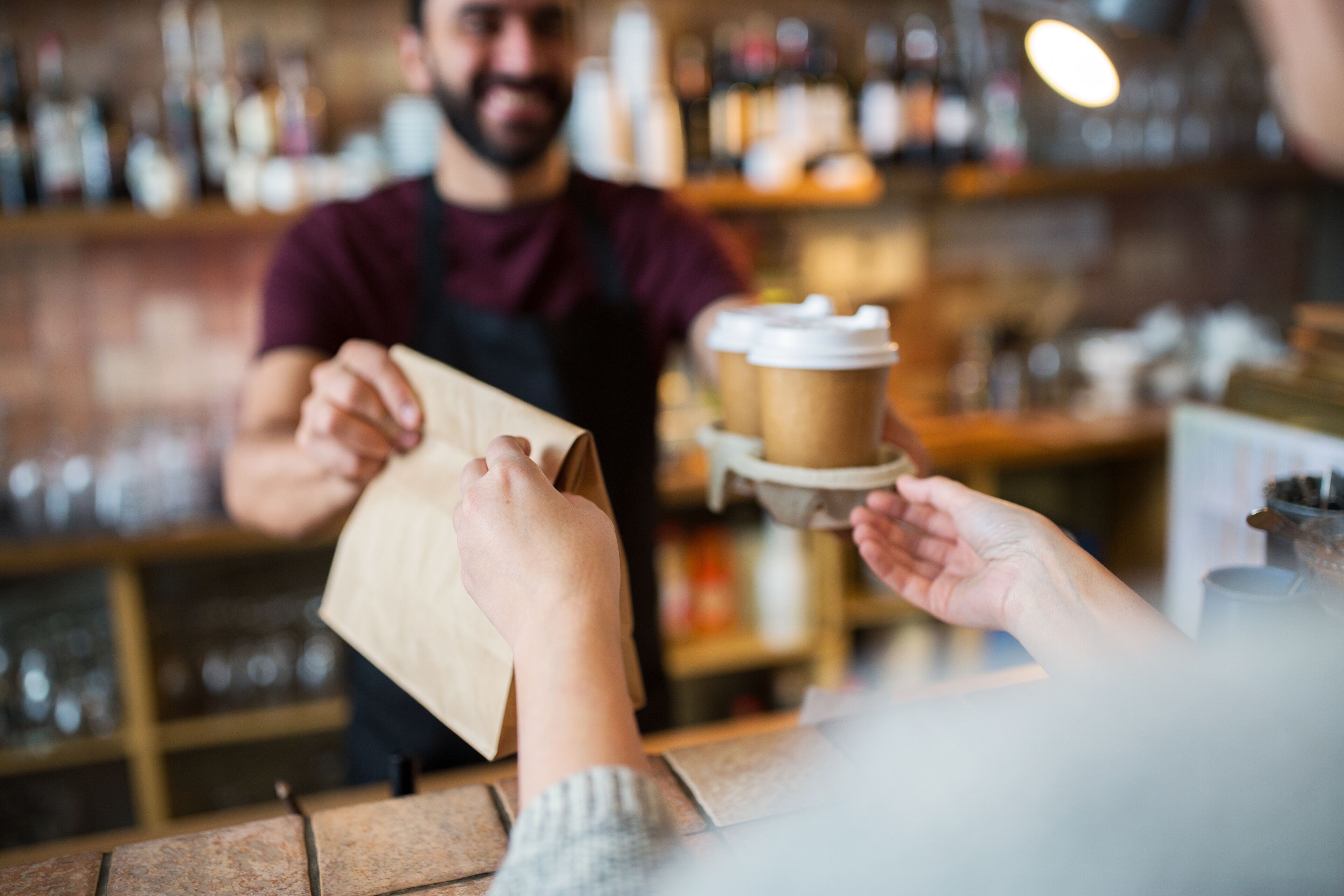 Iemand houdt een papieren tas vast bij een balie, waarschijnlijk in een café of restaurant.