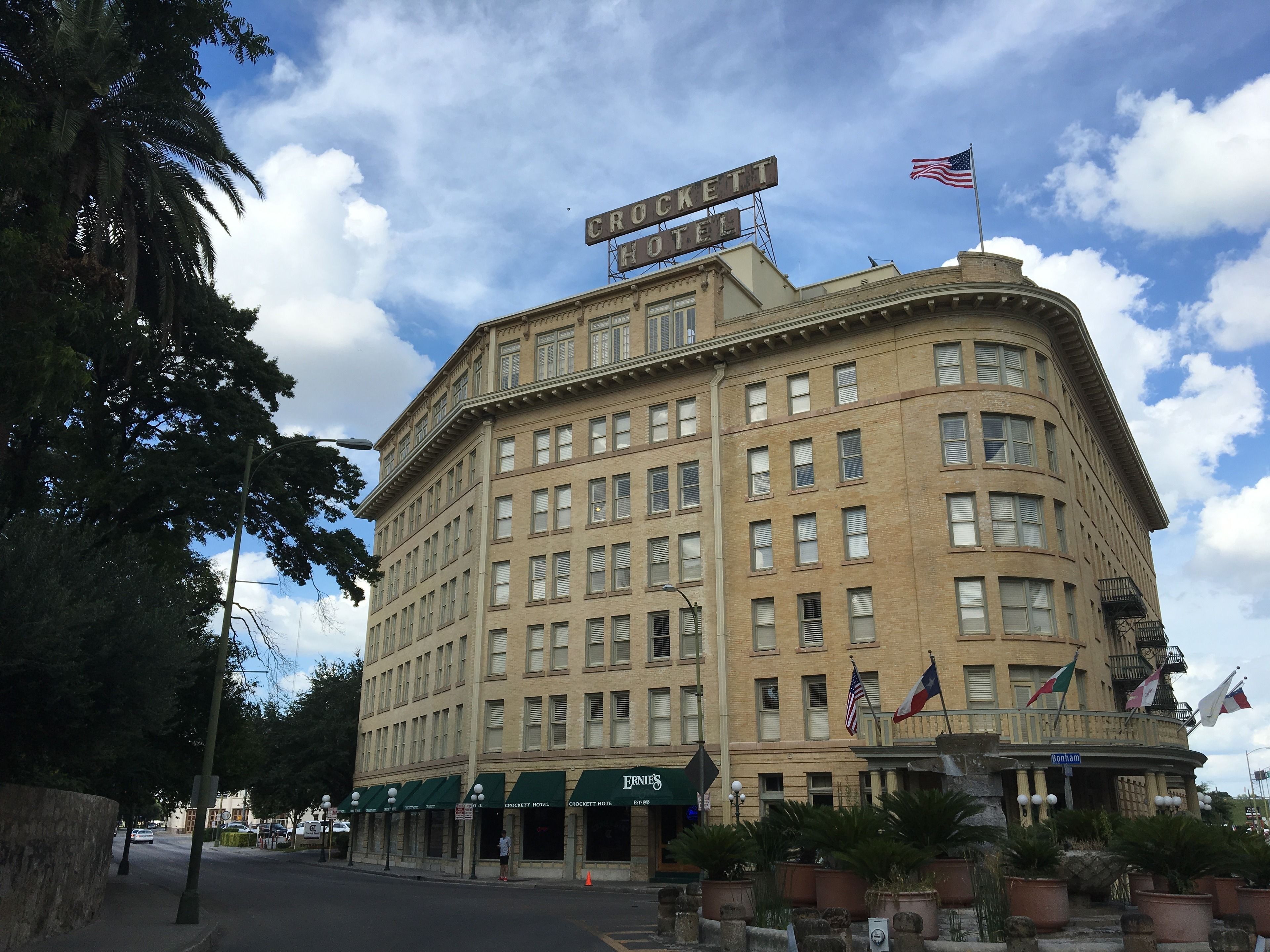 A historic building with multiple stories, a prominent sign reading "Crockett Hotel," and several flags including the American flag.