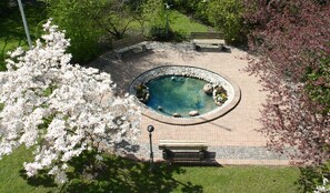 A circular stone pool with a fountain, surrounded by a brick pathway and benches. - Hotel Djingis Khan (Lund)
