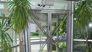 A modern entrance with glass doors, a black mat, and potted plants. - Hotel Djingis Khan (Lund)