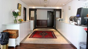 A hotel lobby with a reception desk, a coffee machine, a trash bin, and a decorative rug. - Hotel Djingis Khan (Lund)