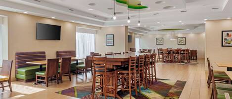 A spacious dining area with multiple tables and booths, a flat-screen TV mounted on the wall, and a patterned rug on the floor.