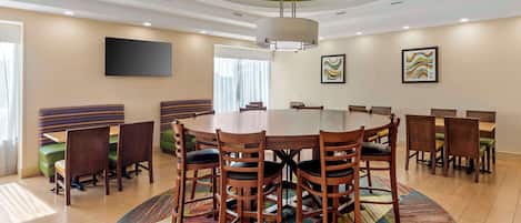 A conference room with a round table, wooden chairs, a colorful rug, and a ceiling light fixture.