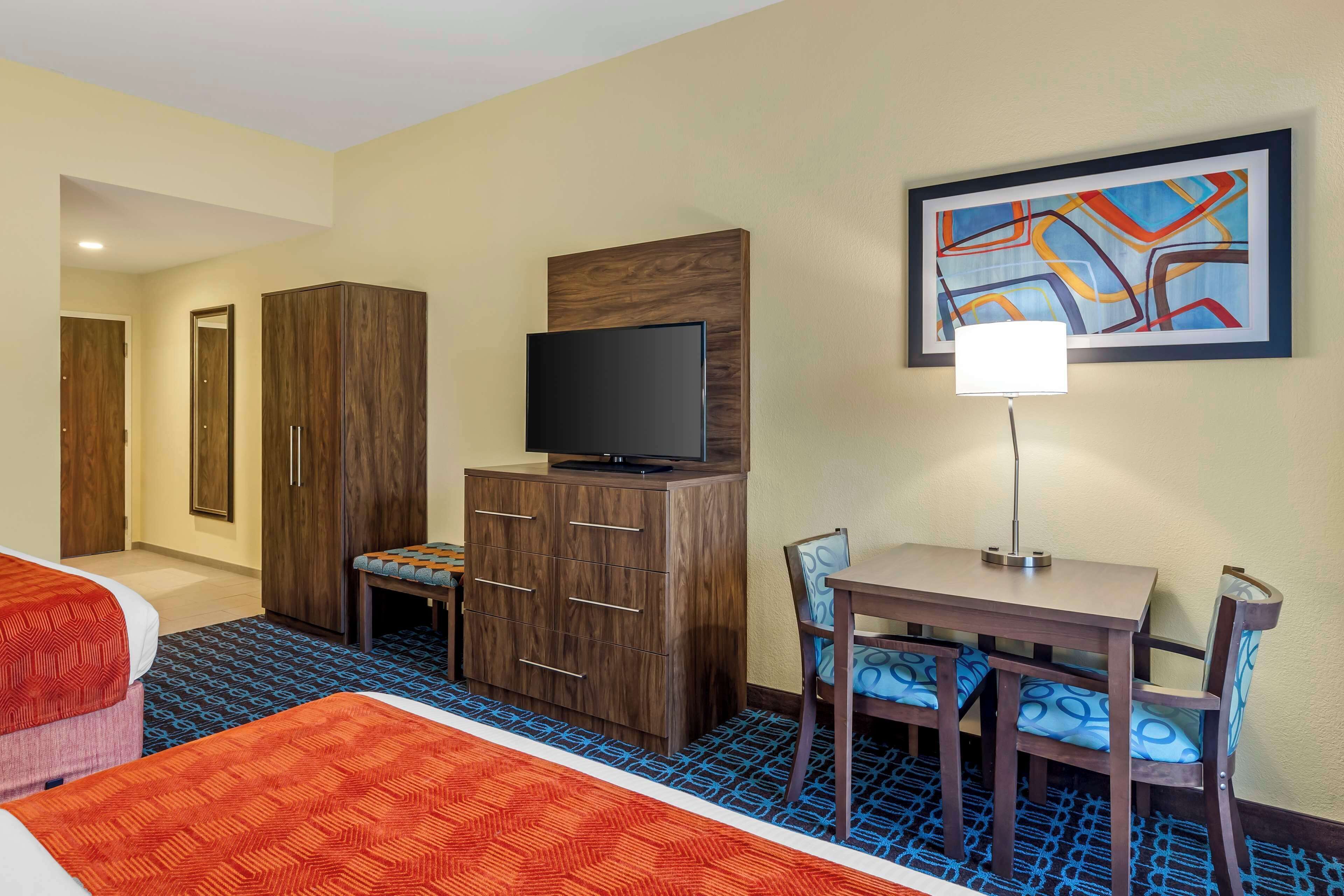 A hotel room with a bed, a desk with a chair, a television, a wardrobe, and a painting on the wall.