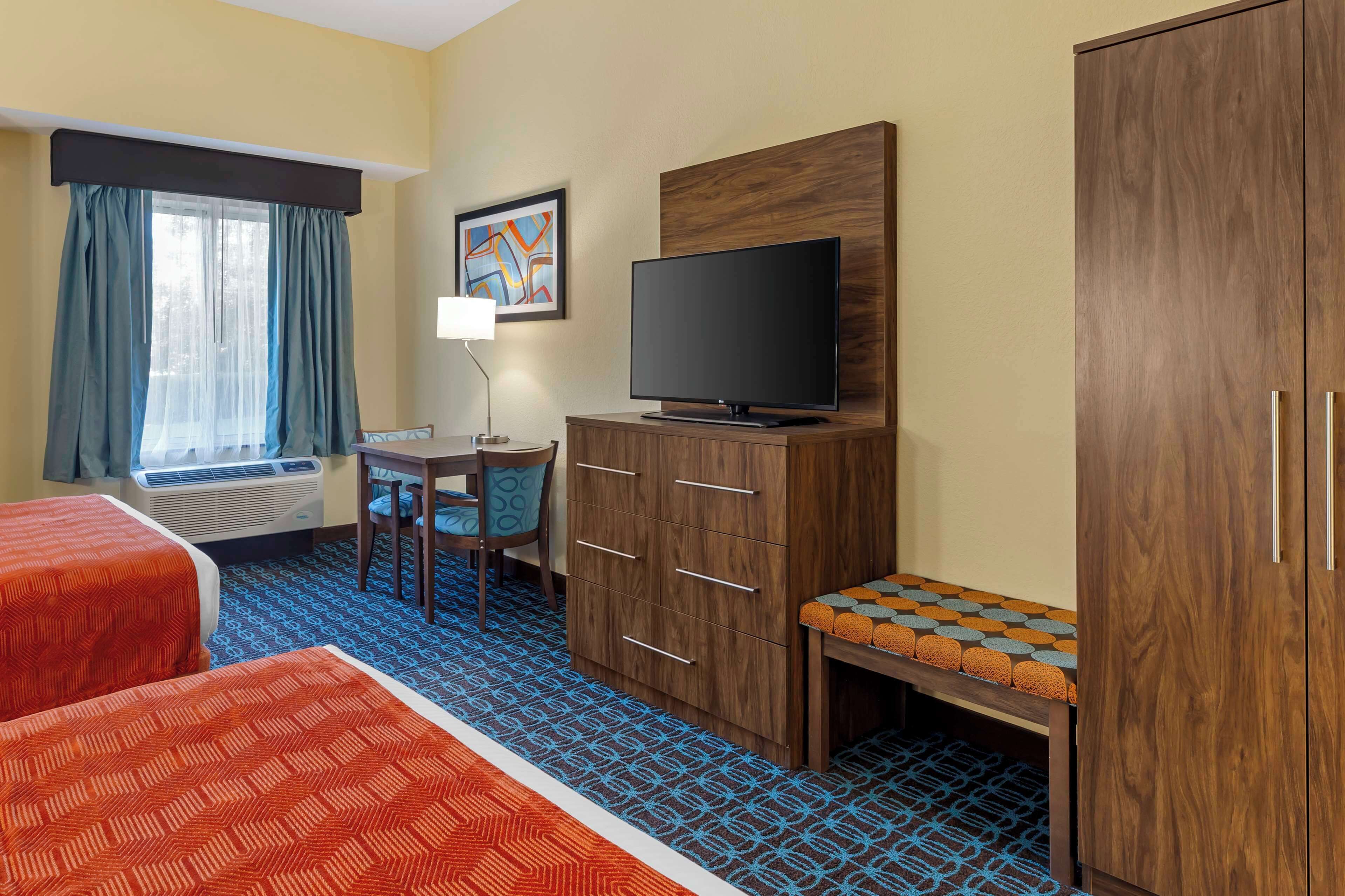 A hotel room with two beds, a desk with a chair, a television, a cabinet, and a window with curtains.