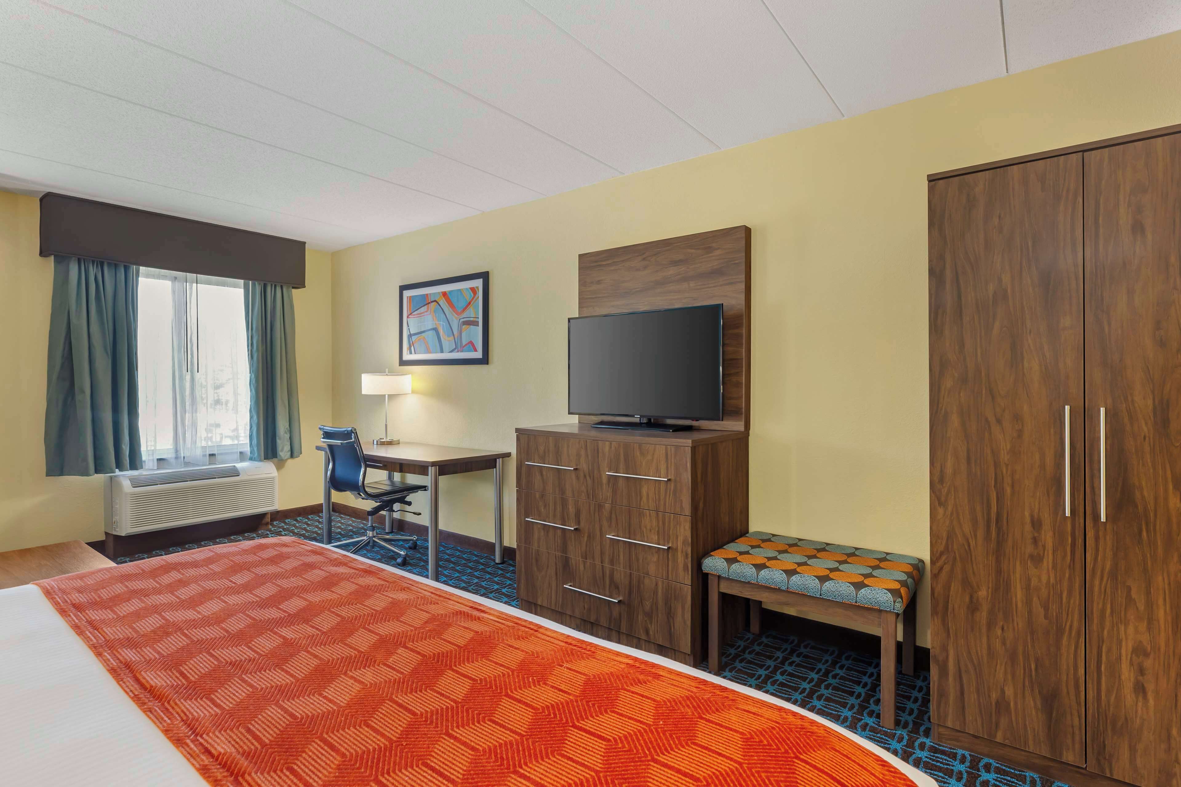Una habitación de hotel con cama, escritorio, televisión, armario y ventana con cortinas.